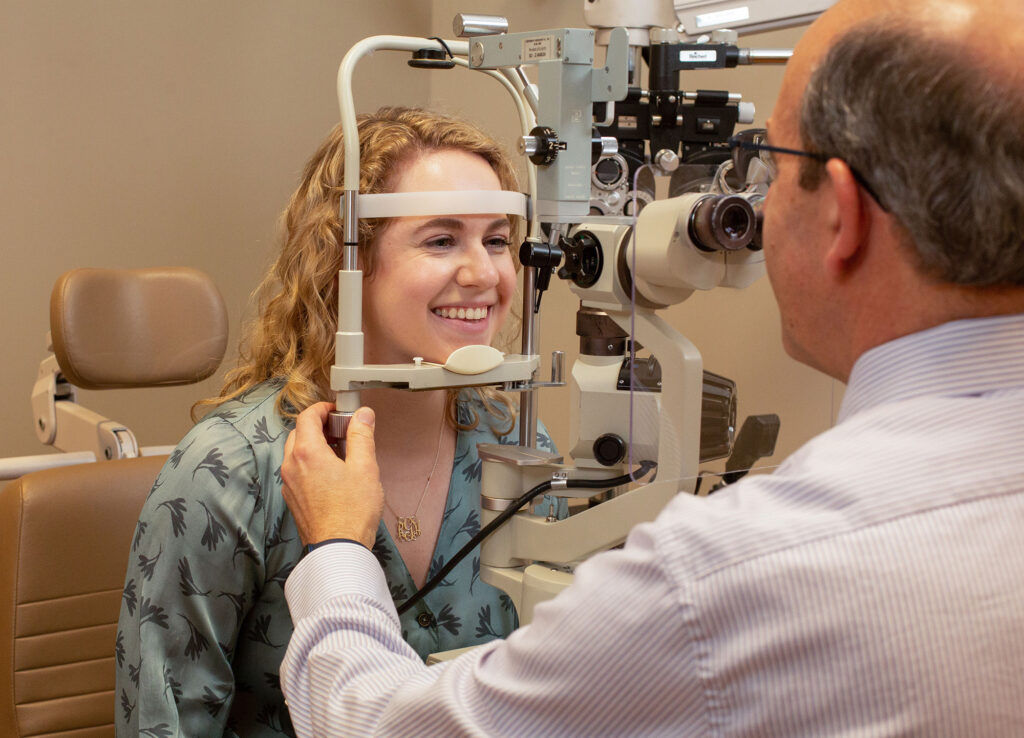 A woman smiles as she rests her head in an eye exam scope.