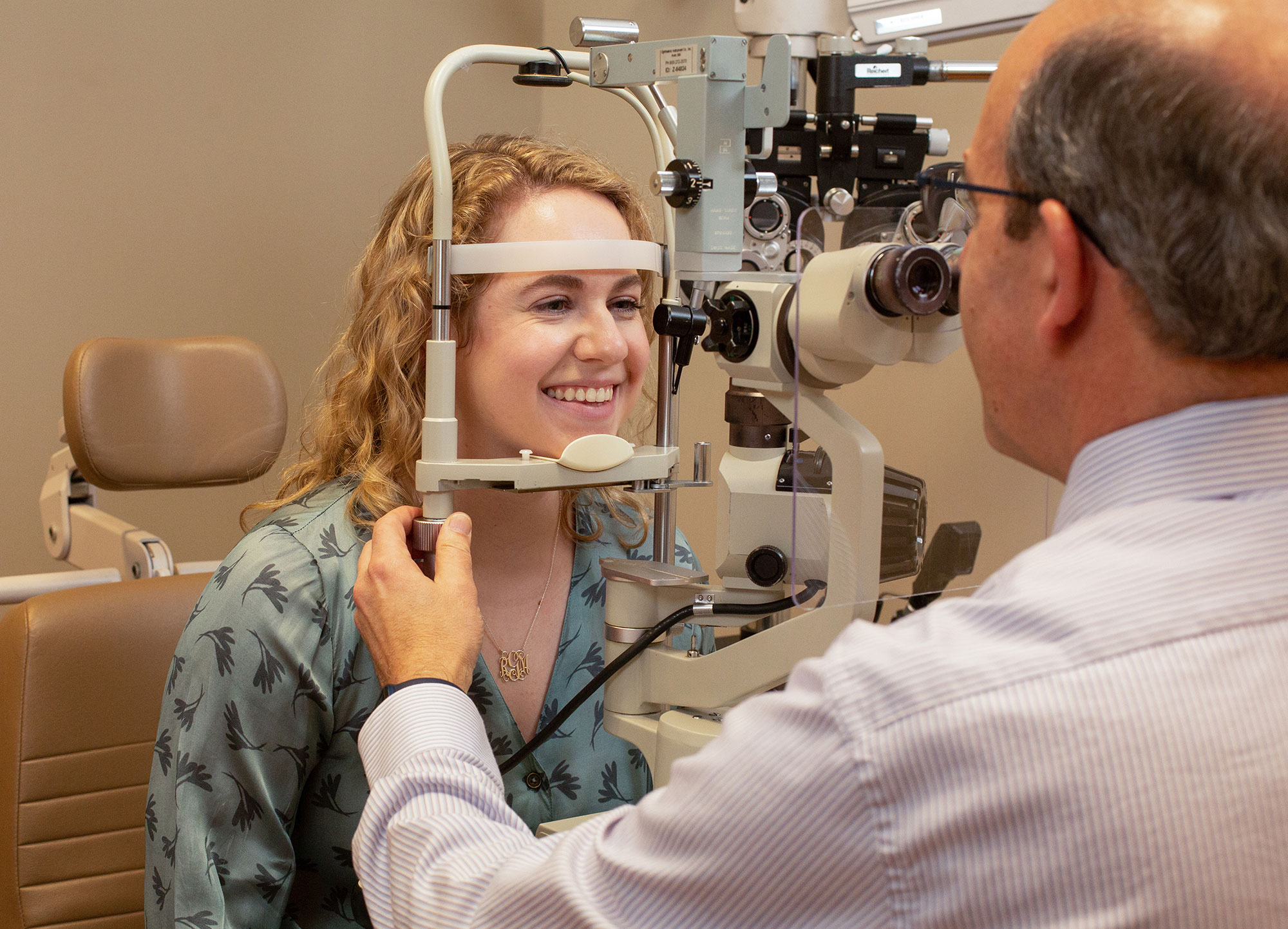 A woman smiles as she rests her head in an eye exam scope. 